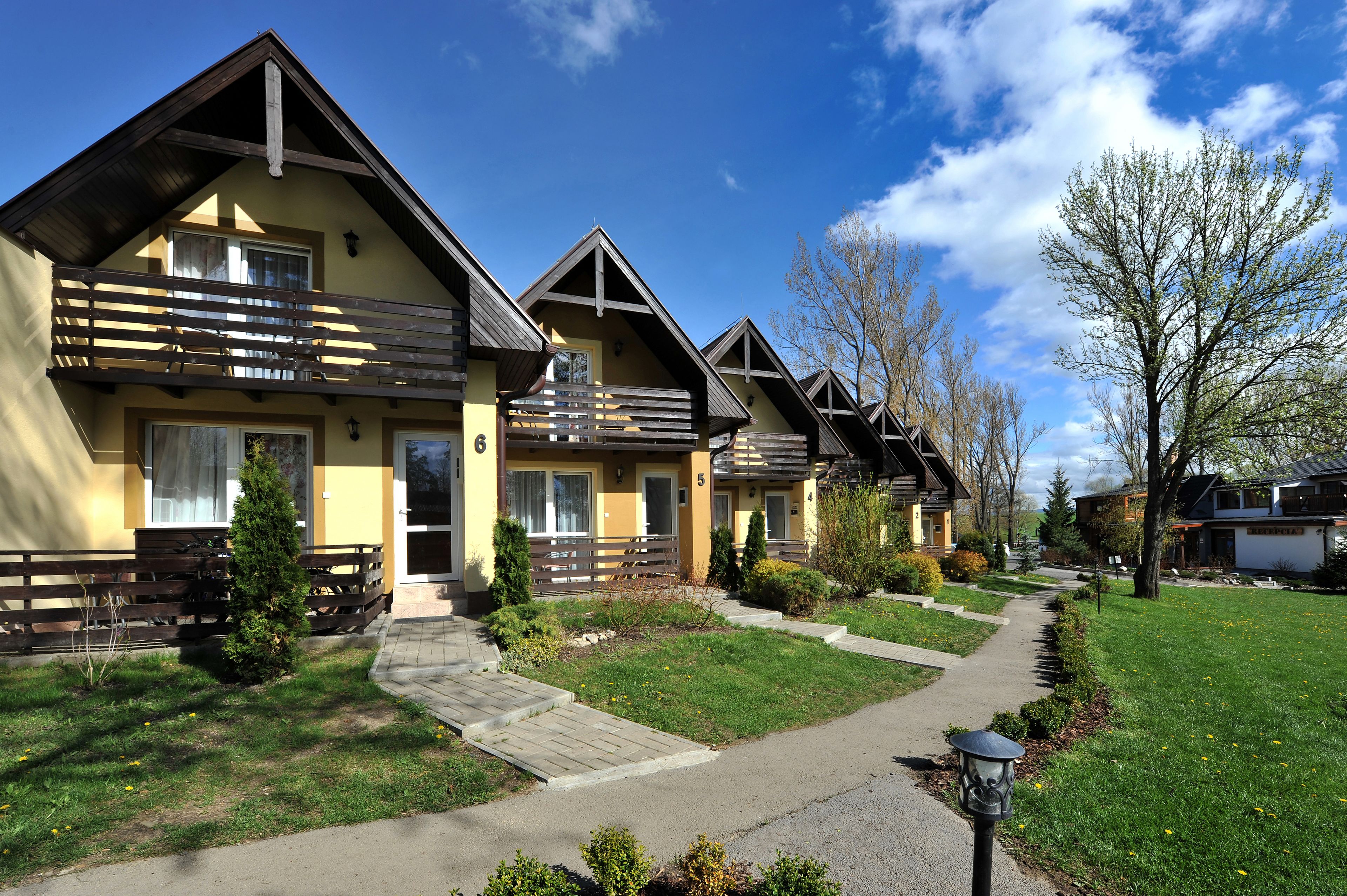 A row of yellow buildings with wooden balconies, a paved walkway, and a clear sky.