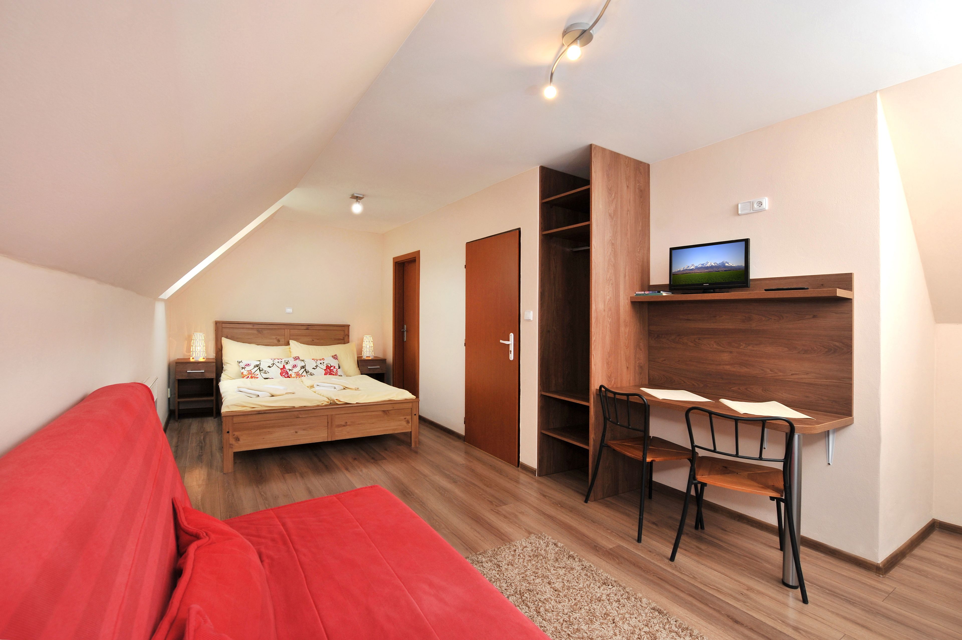 Un dormitorio con cama, mesita de noche, lámpara y televisor en un estante.