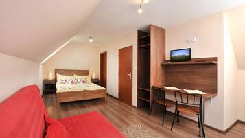 Un dormitorio con cama, mesita de noche, lámpara y televisor en un estante.