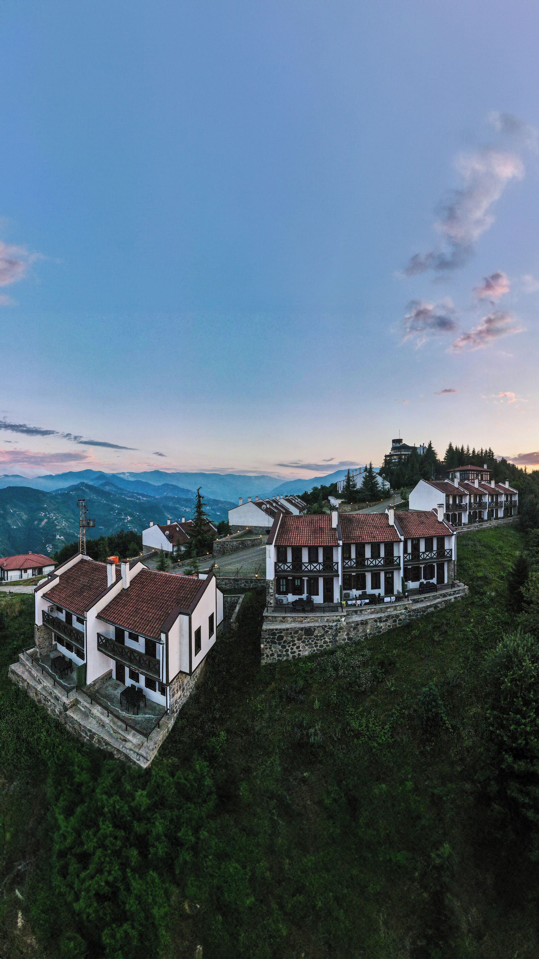 Eine Reihe traditioneller Gebäude mit Steinfundament vor einer Bergkulisse und blauem Himmel.
