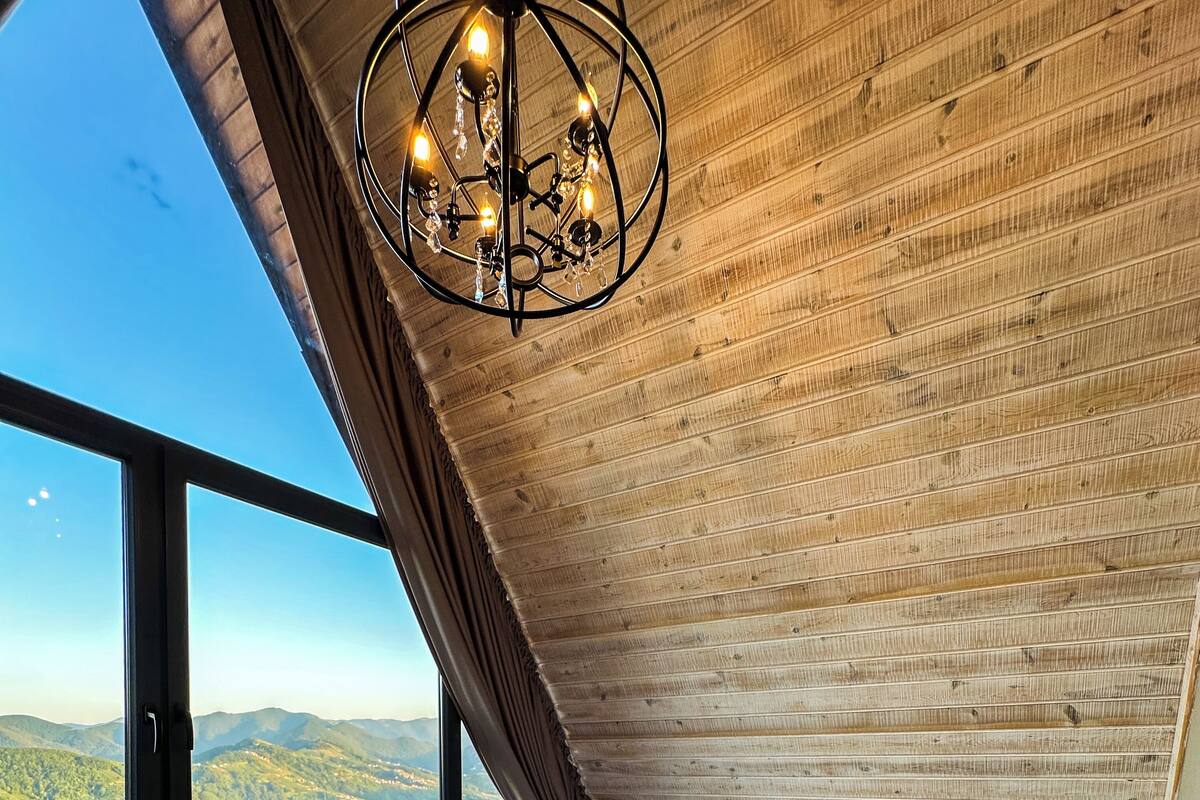 A bedroom with a large window, a bed, a nightstand, and a chandelier.