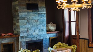 Una habitación acogedora con chimenea de piedra, dos sillones tapizados, techo de madera y una lámpara colgante.