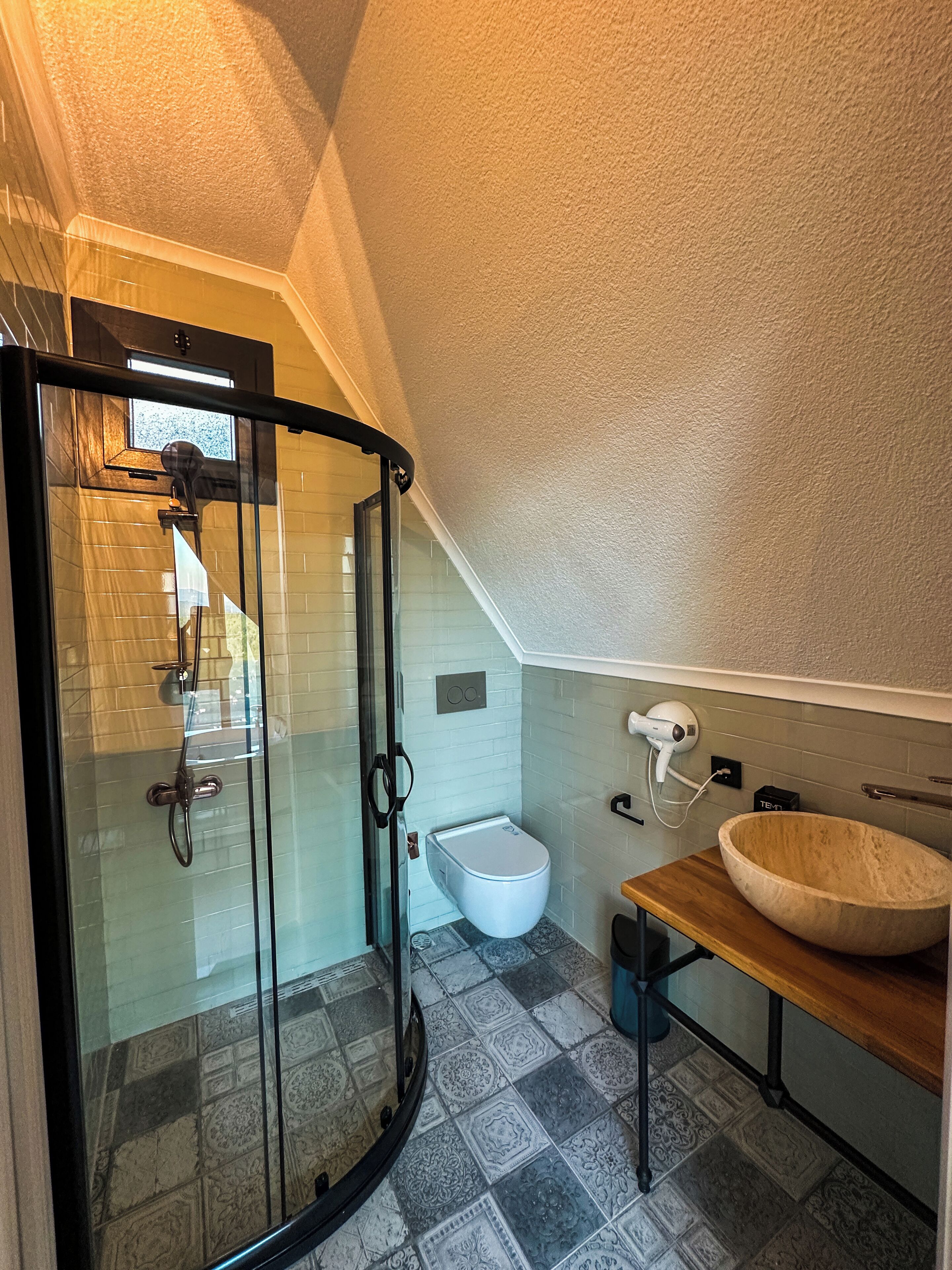 A modern bathroom with a glass shower enclosure, a white toilet, and a wooden vanity with a large bowl sink.