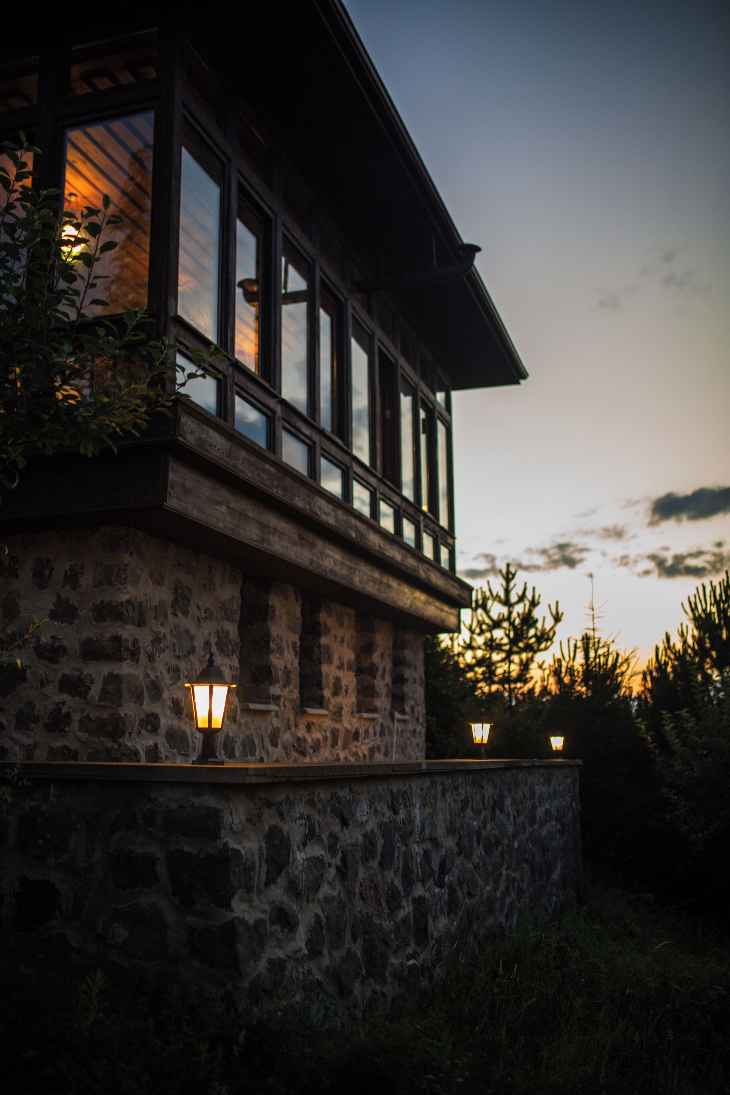 A stone building with large windows and a balcony, featuring exterior lighting.