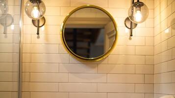 Un baño con un espejo redondo, dos luces empotradas, un grifo negro, un lavabo de piedra y un perchero con toallas.