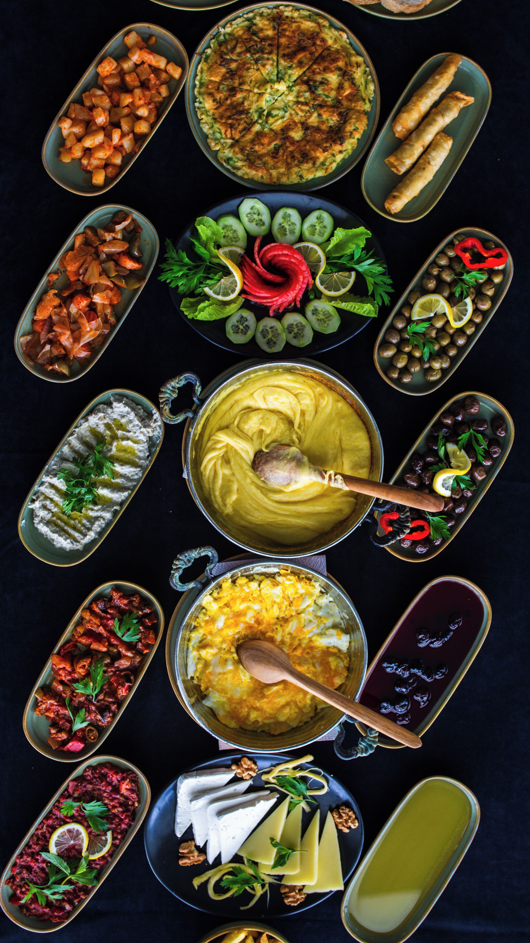 Variedad de platos dispuestos en una mesa, incluyendo una olla de sopa, un plato de verduras y varios recipientes pequeños con diferentes alimentos.