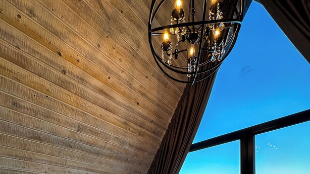Un baño moderno con una bañera grande, techo de madera y vistas a un paisaje verde a través de grandes ventanales.