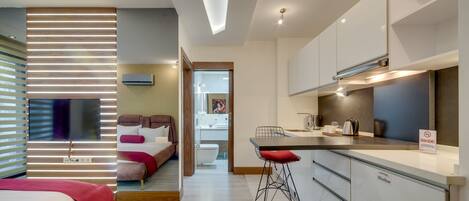 Quarto de hotel moderno com cama, escrivaninha, cozinha compacta e banheiro.