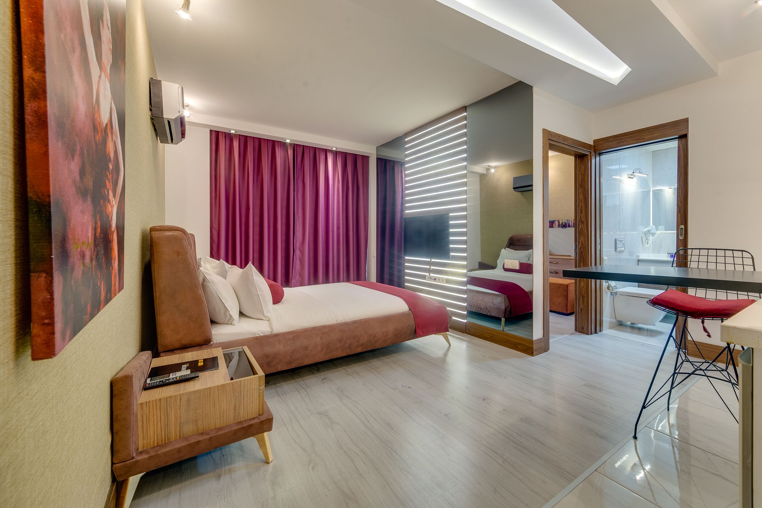 Ett modernt hotellrum med en säng, en liten sittgrupp, ett glasbord och ett badrum som syns genom en glasdörr.