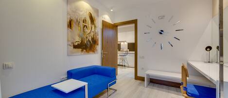 Una habitación moderna con un sofá azul, una mesa blanca, una silla de madera y un cuadro abstracto grande en la pared.