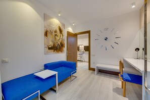 A modern room with a blue sofa, a white table, a wooden chair, and a large abstract painting on the wall. - Concept Suites (Aydin)