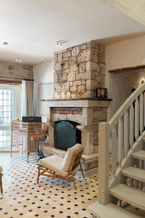 A stone fireplace, a wicker chair, a television, and a staircase. - Palm Alaçatı Boutique Hotel (Cesme)