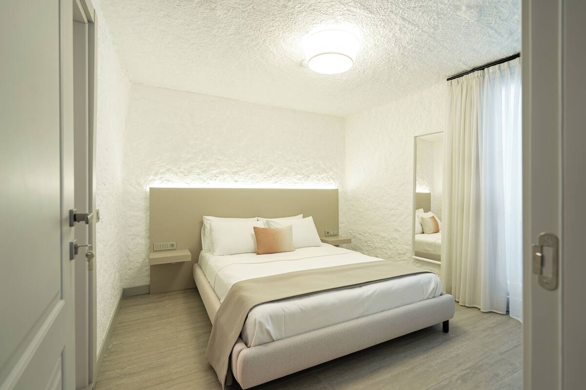 Hotellihuone, jossa on sänky, yöpöydät, peili ja ovi.