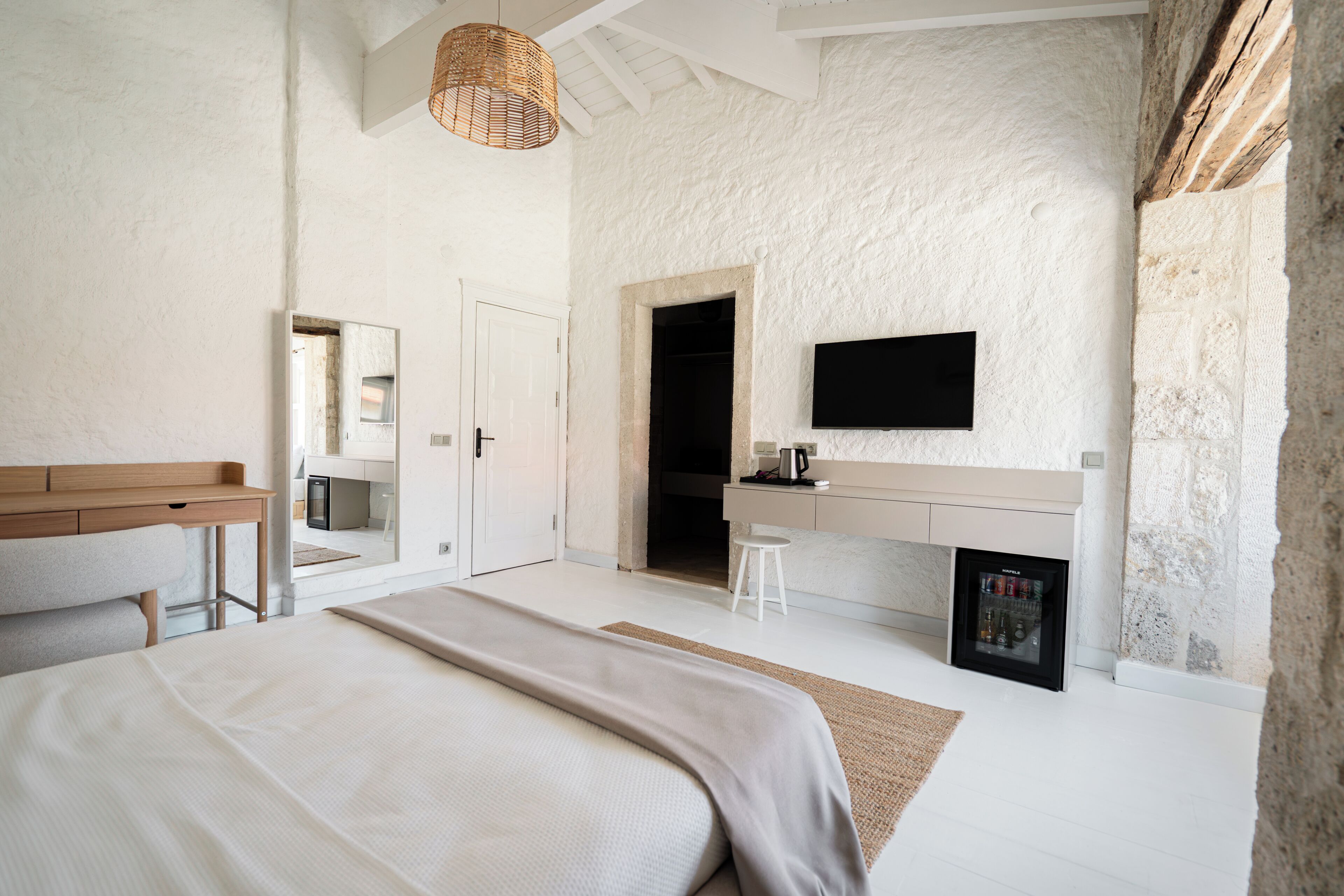 A bedroom with a bed, a desk, a chair, a television, and a minibar.