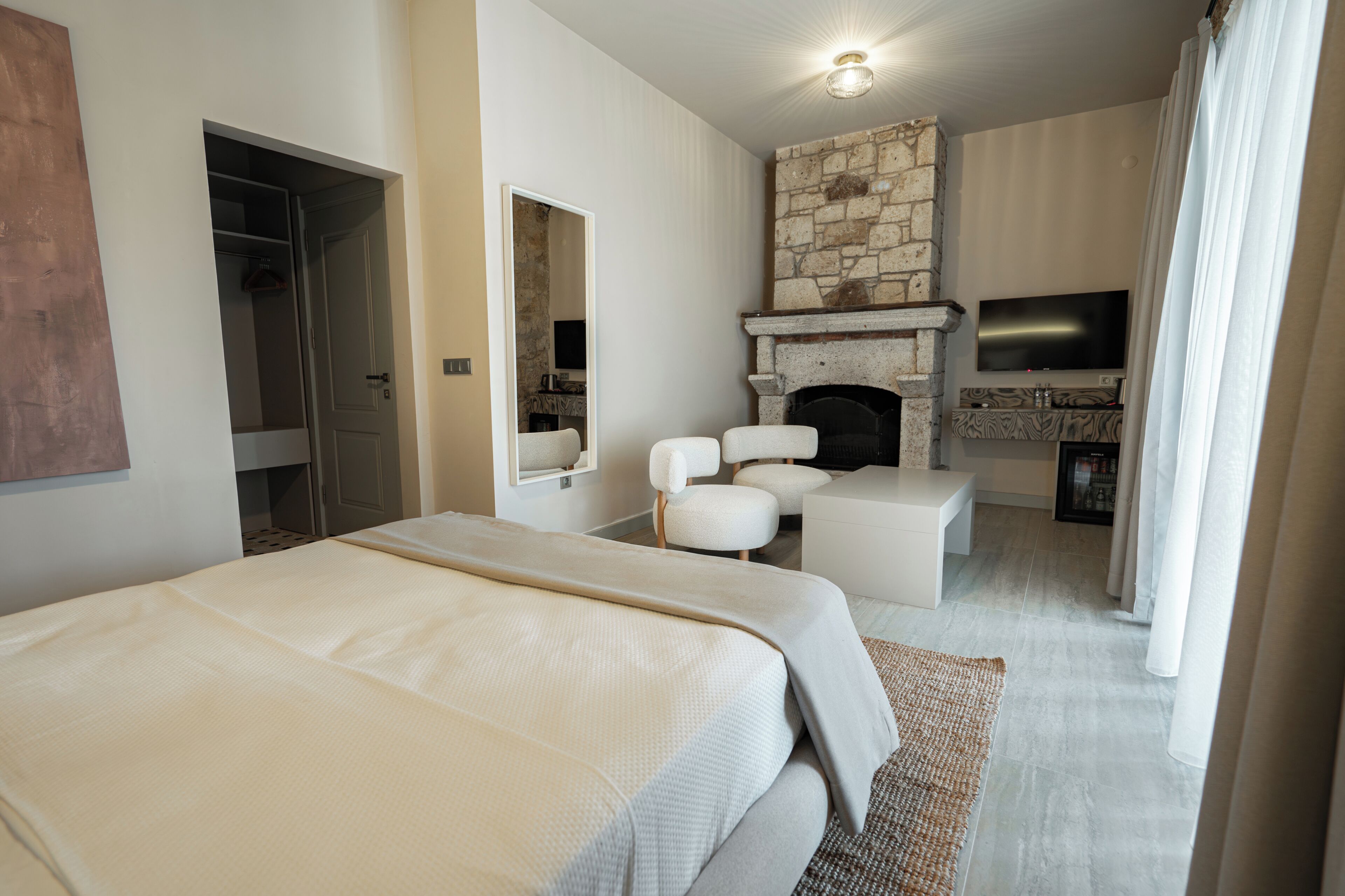 Una habitación de hotel moderna con una cama grande, una zona de estar con sillones, una chimenea de piedra y un televisor de pantalla plana.