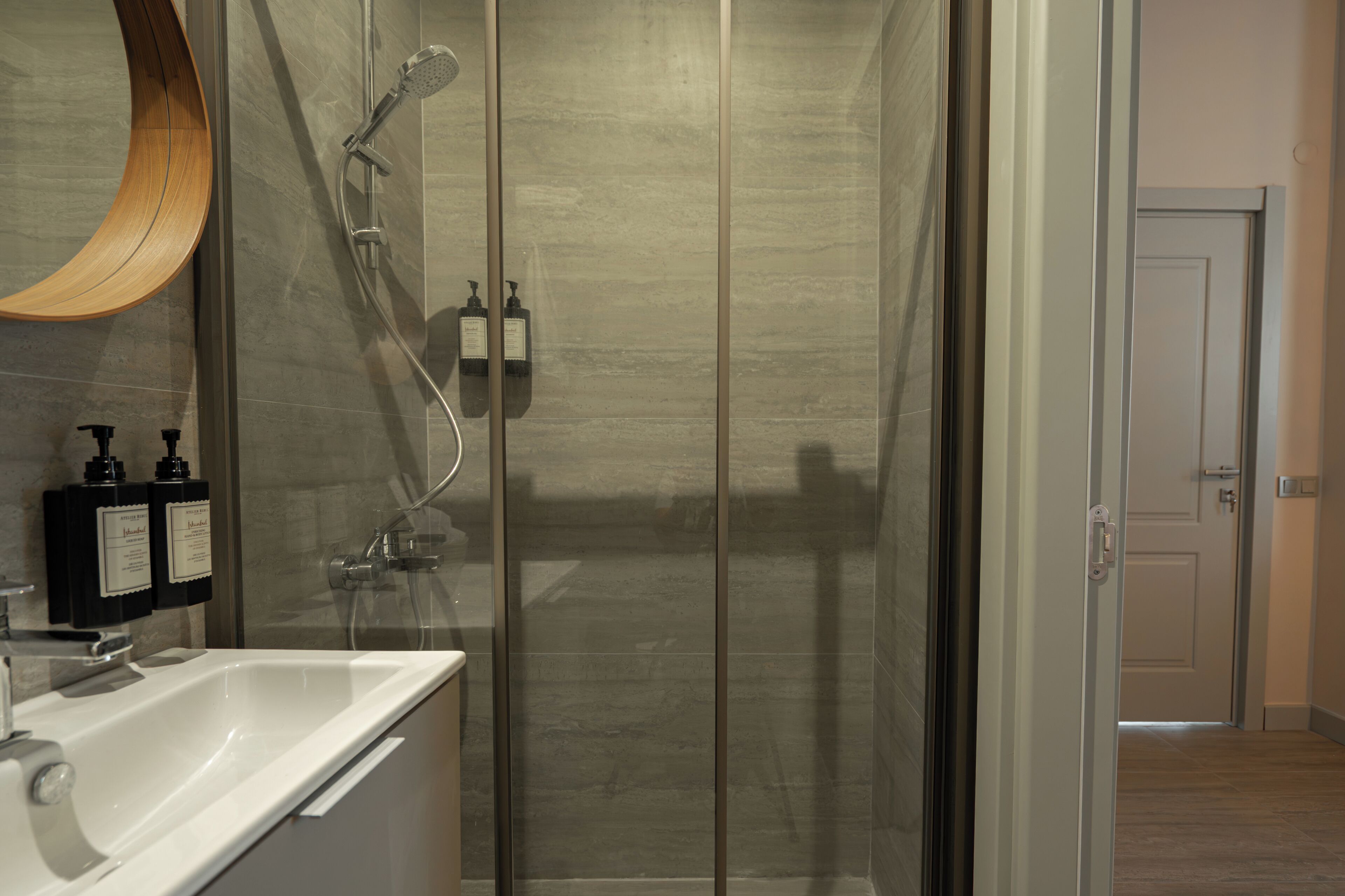 A modern bathroom with a glass shower enclosure, a white sink, and two bottles of shampoo on the wall.