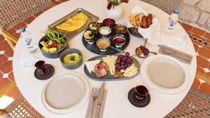 Ein runder Tisch mit einer Auswahl an Speisen, darunter Käse, Früchte und Brot, für eine Mahlzeit angerichtet.