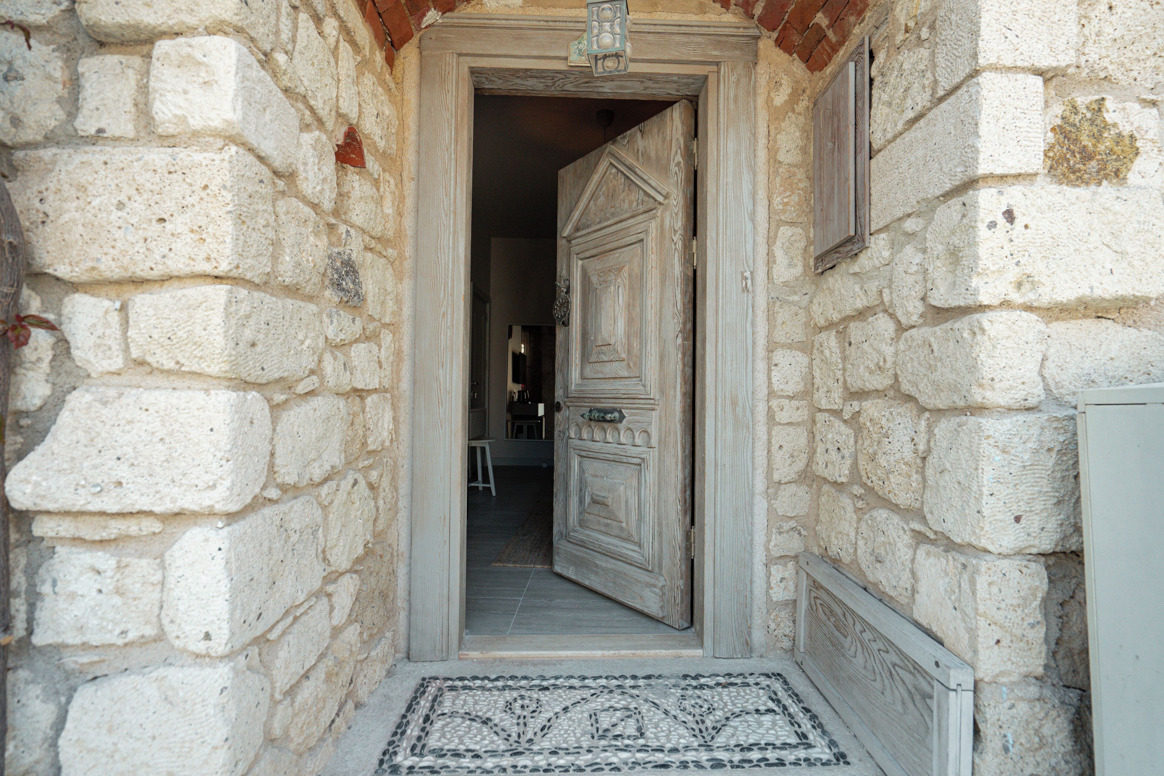 A stone building entrance with a door, a small window, and a tiled floor.