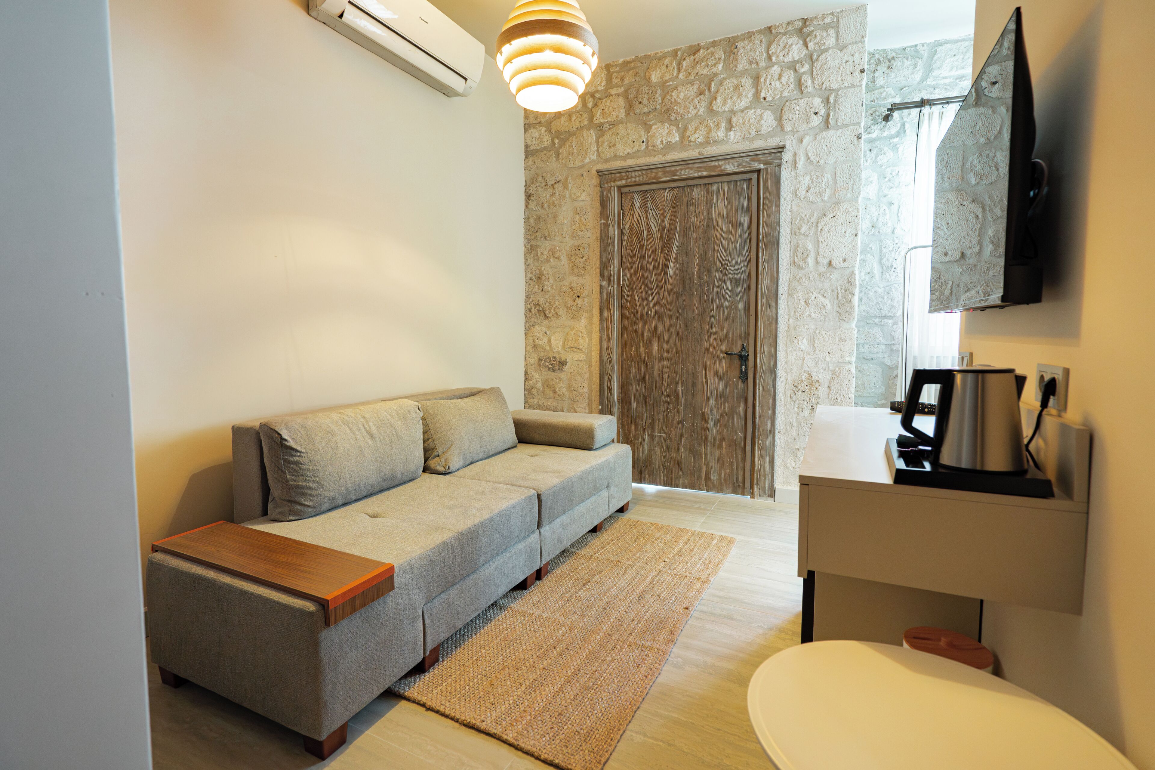A modern living room with a sofa, a wooden coffee table, a TV mounted on the wall, and a stone wall.