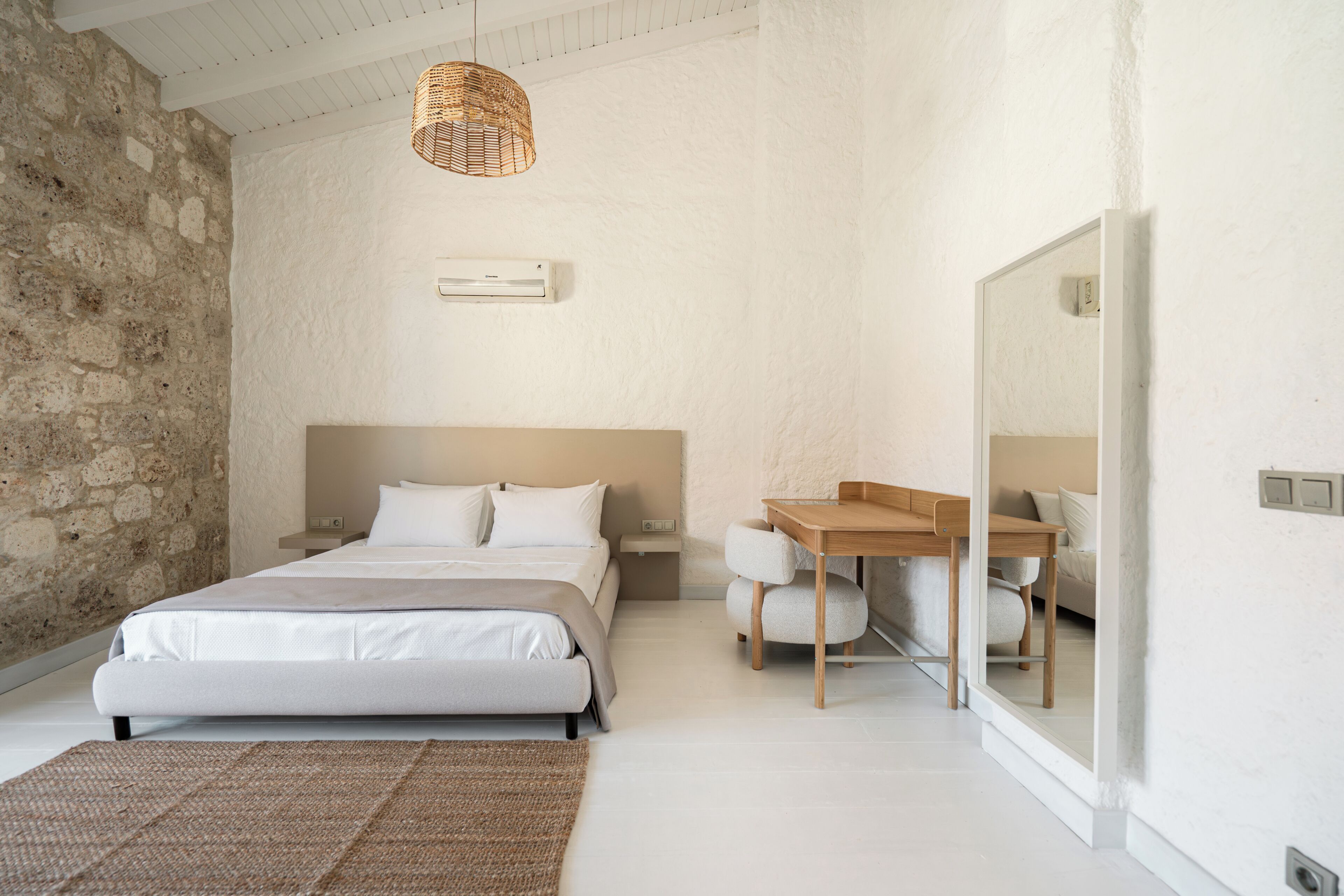 A bedroom with a bed, bedside table, wooden desk, and a large mirror.
