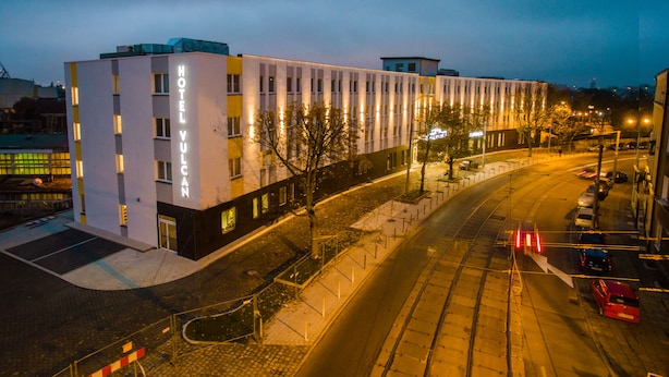 A modern hotel building with a prominent sign, a paved street, and parked cars. - Vulcan Hotel (Szczecin)