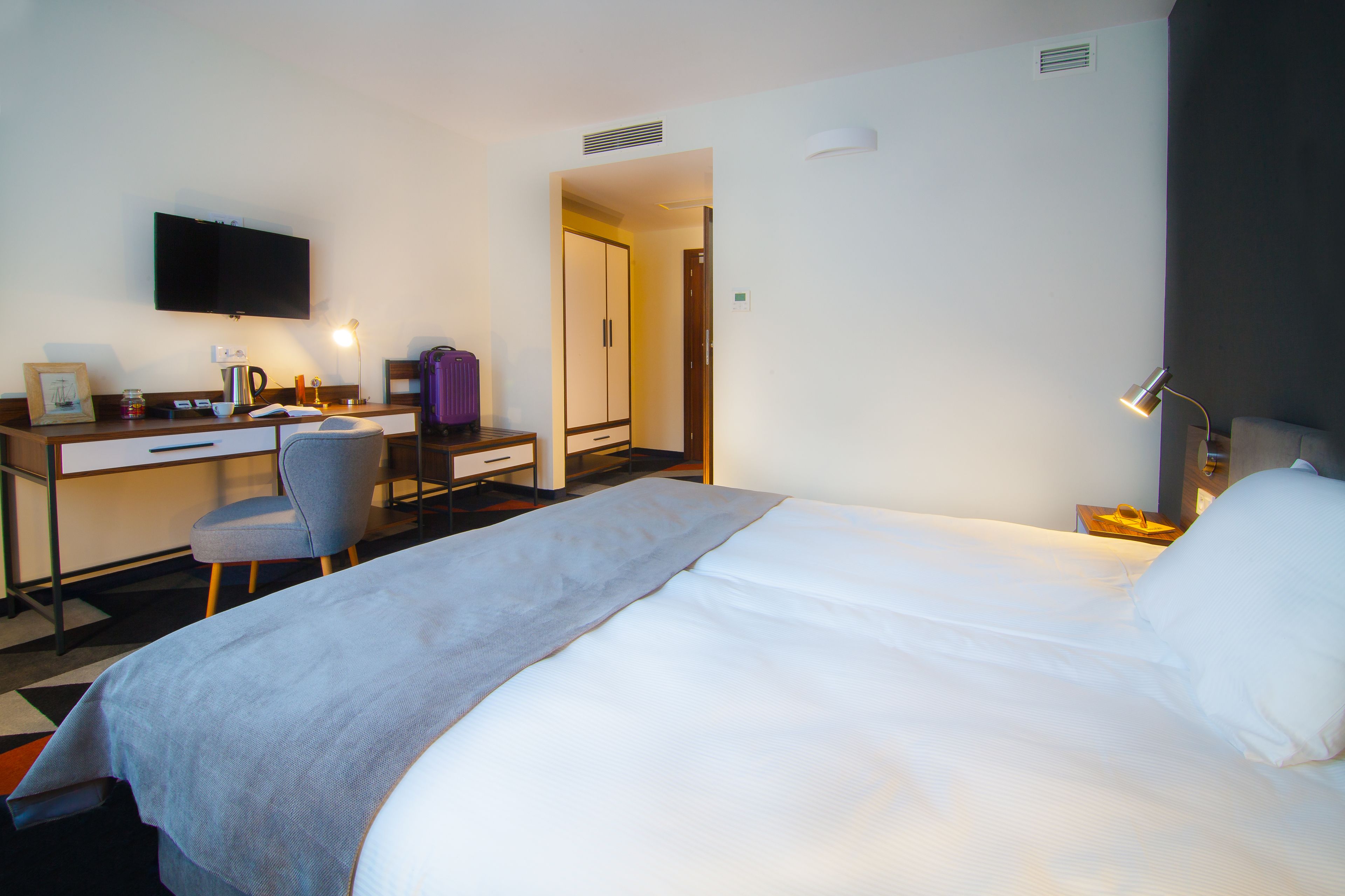 Una camera d'albergo con un letto, una scrivania con sedia, una televisione e una lampada.