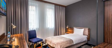 Habitación de hotel con cama, escritorio, silla y ventana grande con cortinas.