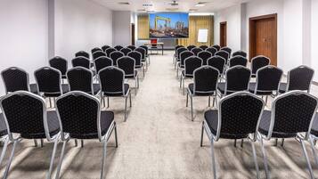 A conference room with rows of black chairs, a projector screen, and a presentation area.