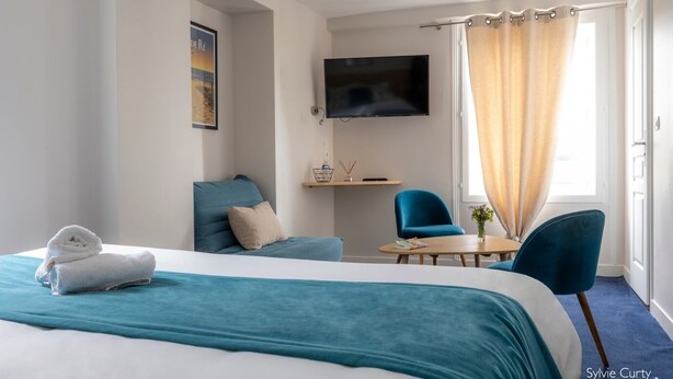 A hotel room with a bed, two chairs, a TV, and a window with curtains. - Un Hôtel sur le Port (La Rochelle)
