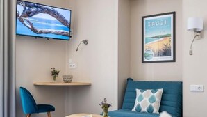 A modern living room with a sofa, a TV, and a small table. - Un Hôtel sur le Port (La Rochelle)
