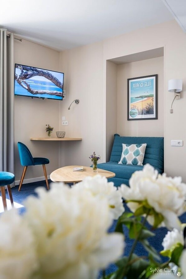 A modern living room with a sofa, a TV, and a small table. - Un Hôtel sur le Port (La Rochelle)