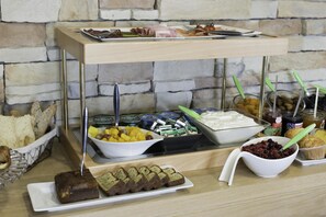 A buffet setup with various food items, including bread, fruits, and desserts, arranged on a wooden table against a stone wall. - Un Hôtel sur le Port (La Rochelle)