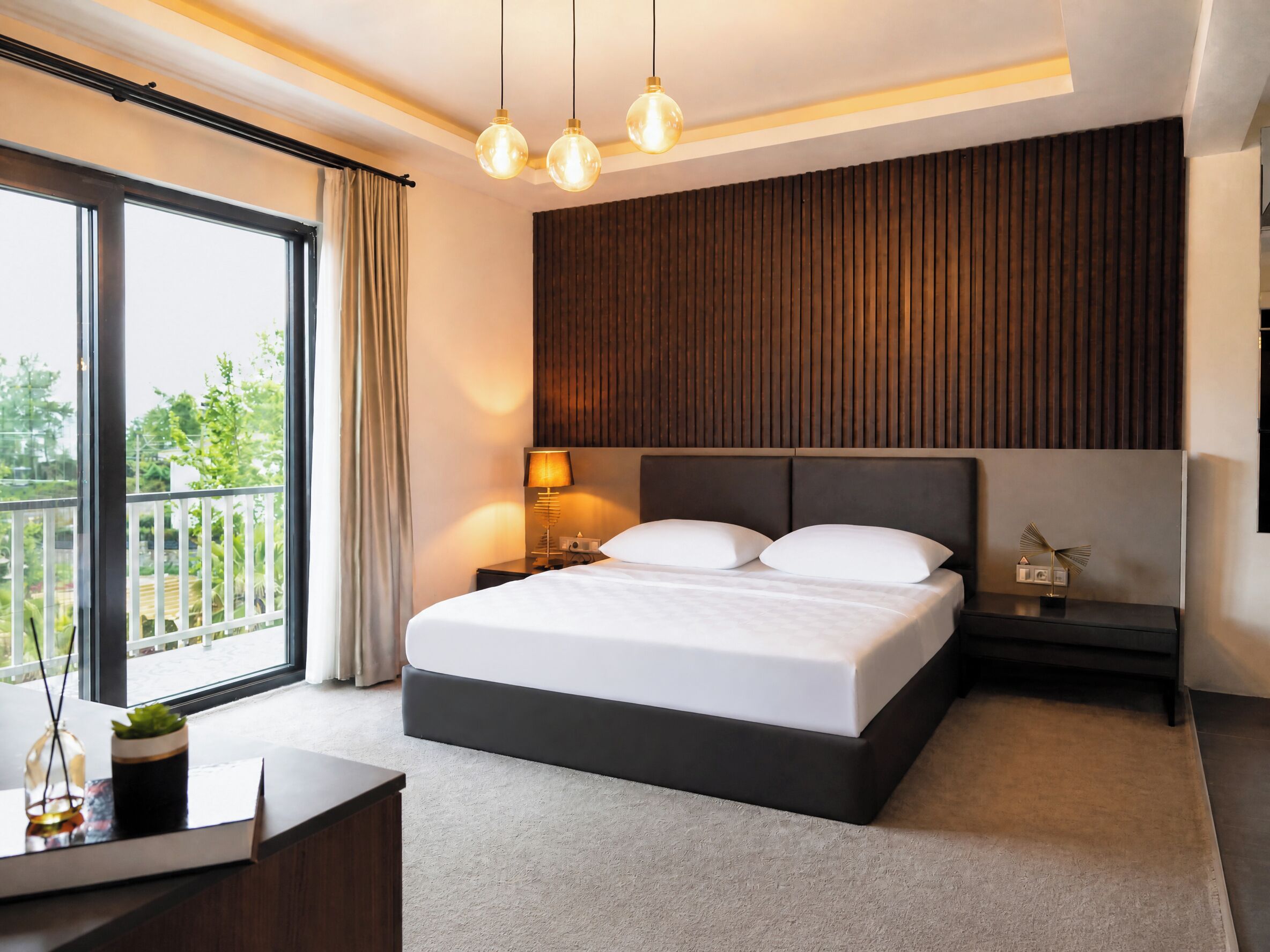 Une chambre d’hôtel moderne, dotée d’un grand lit, de tables de chevet, d’une lampe et offrant une vue sur la verdure environnante.