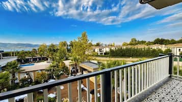 Un balcón con vista a una piscina, un área de comedor y edificios circundantes.