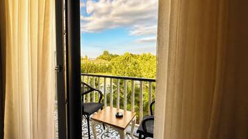 A balcony with a table and chairs, a view of greenery, and a partly cloudy sky.