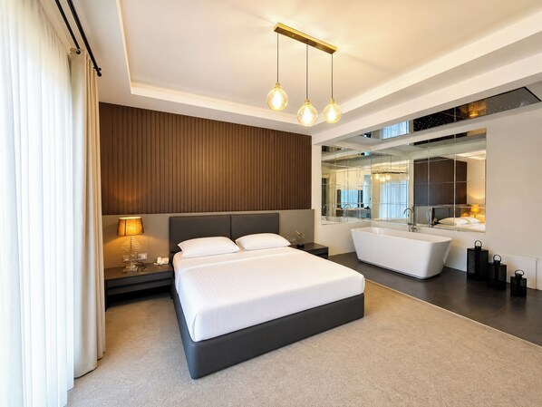 Ein modernes Hotelzimmer mit einem großen Bett, einer integrierten Badewanne, einem Schminktisch mit Spiegel und einer Deckenleuchte.