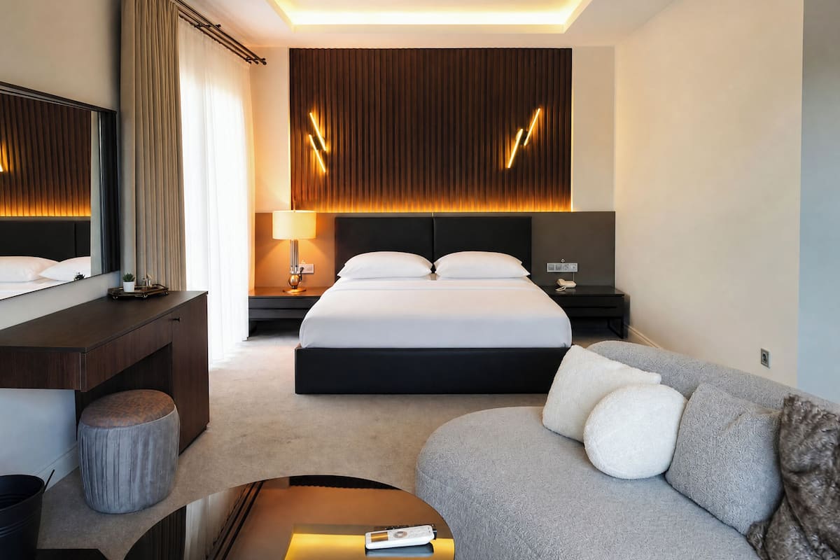 Una habitación de hotel moderna con una cama grande, un sofá, un escritorio y un espejo.