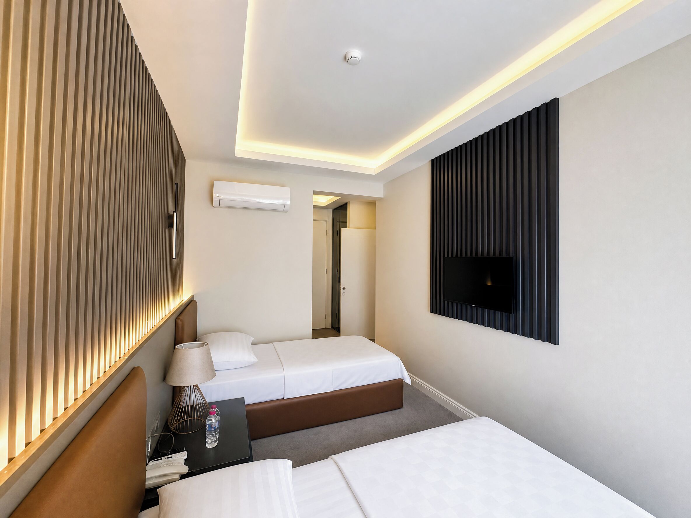 A hotel room with two beds, a TV, an air conditioner, and a lamp.