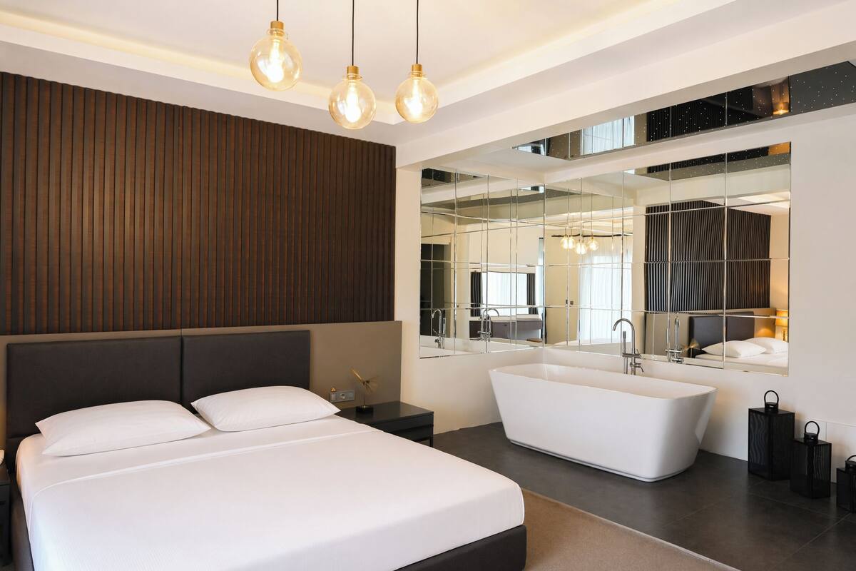 Ein modernes Schlafzimmer mit einem großen Bett, einer freistehenden Badewanne und einem großen Spiegel, der den Raum widerspiegelt.
