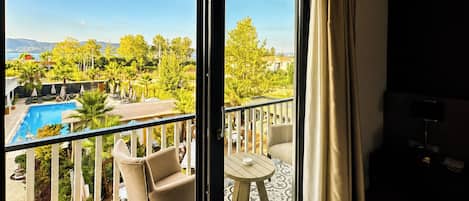 A balcony with a pool, outdoor furniture, and a view of a landscape with trees and a distant body of water.