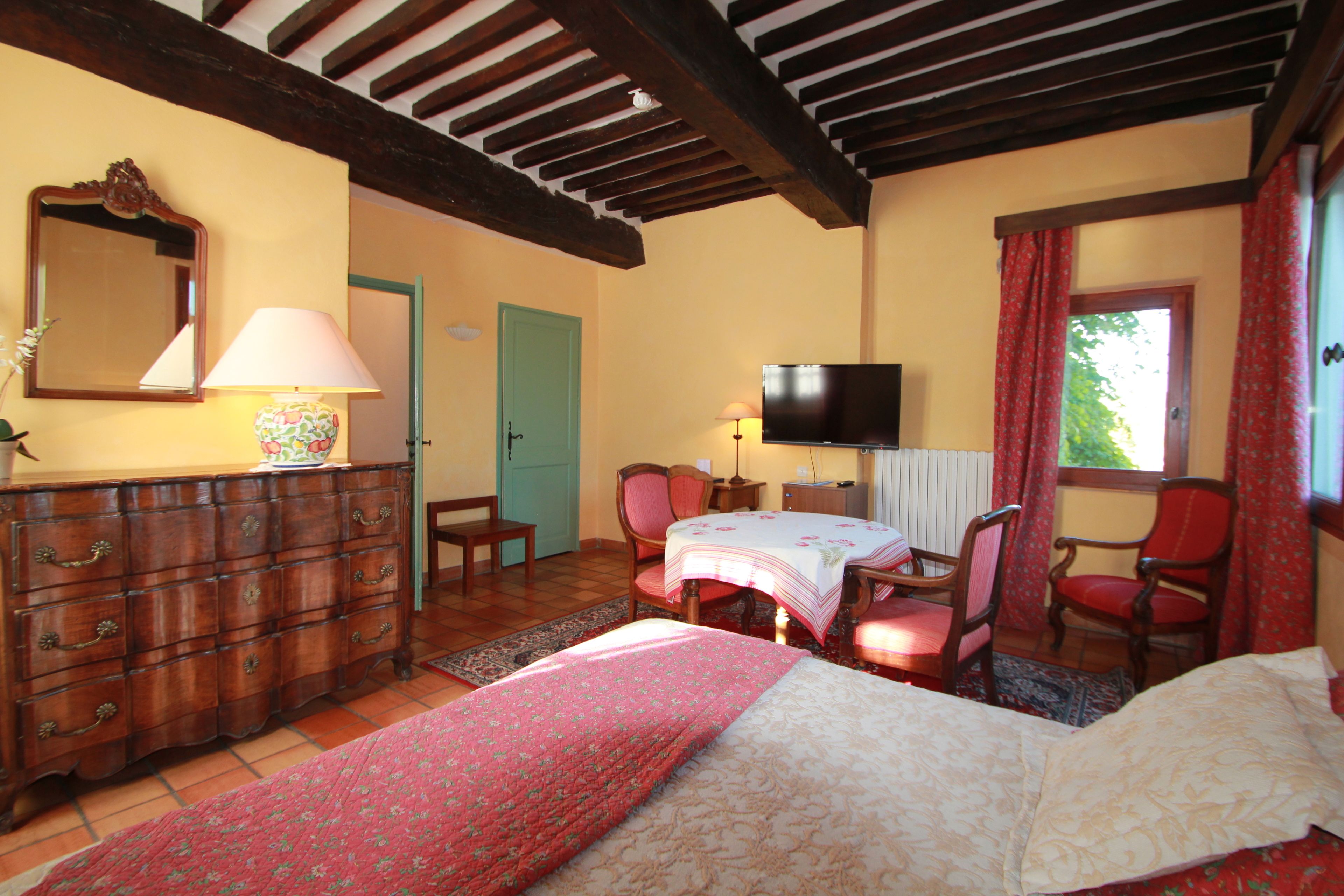 Une chambre à coucher comprenant un lit, une commode, des chaises, un téléviseur et une fenêtre avec des rideaux.
