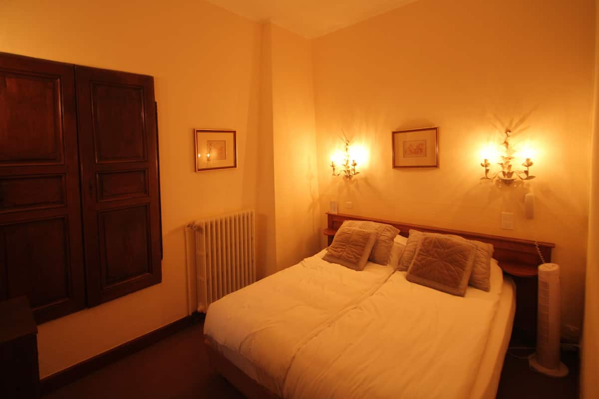 Une chambre à coucher avec un grand lit, deux tables de chevet, un radiateur et deux lampes fixées au mur.