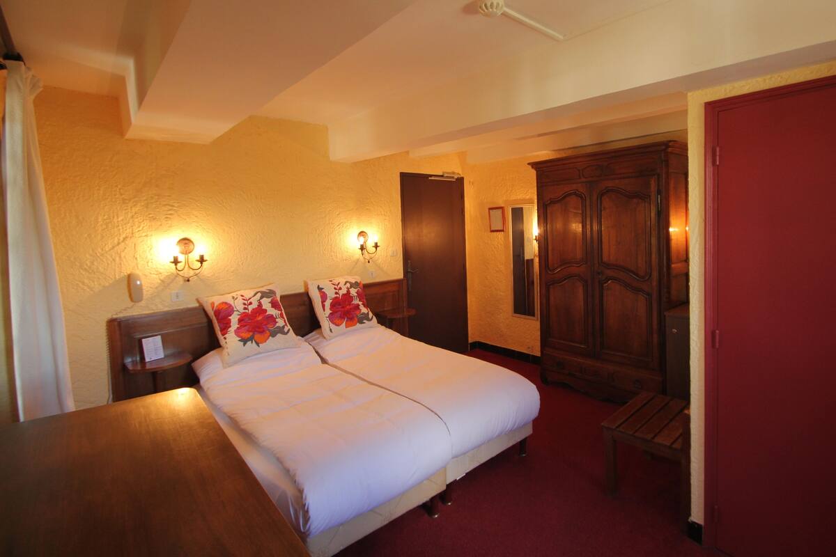 Une chambre d’hôtel avec un lit double, des tables de chevet, un banc, une armoire et des lampes fixées au mur.