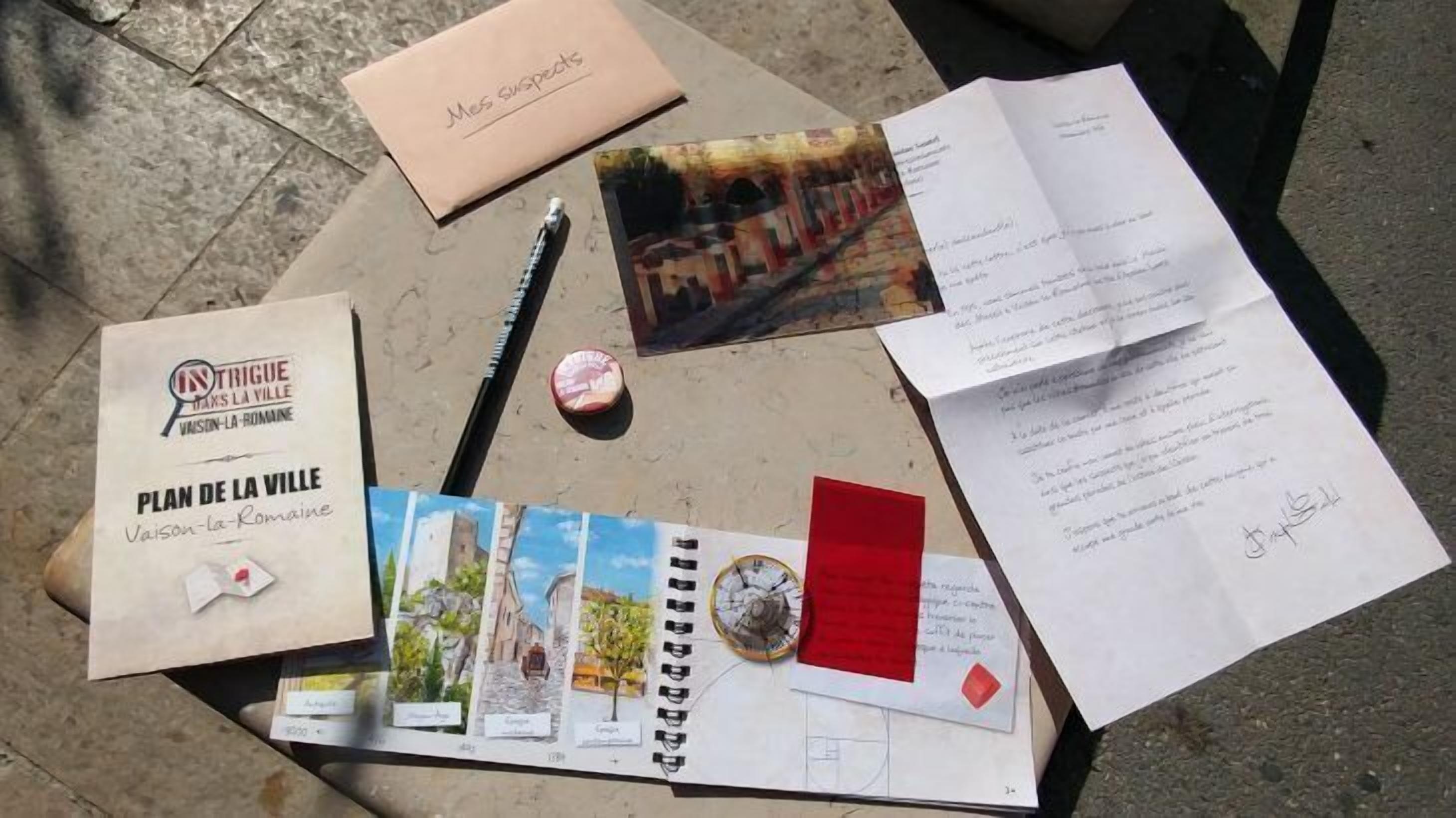 A table with various travel-related items including a booklet titled 'Plan de la Ville', a postcard, a pen, a small box, and some papers.