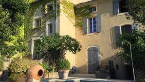 A poolside view of a Mediterranean-style building with a pool, potted plants, and a rustic barrel. - Hostellerie Le Beffroi (Vaison-la-Romaine)