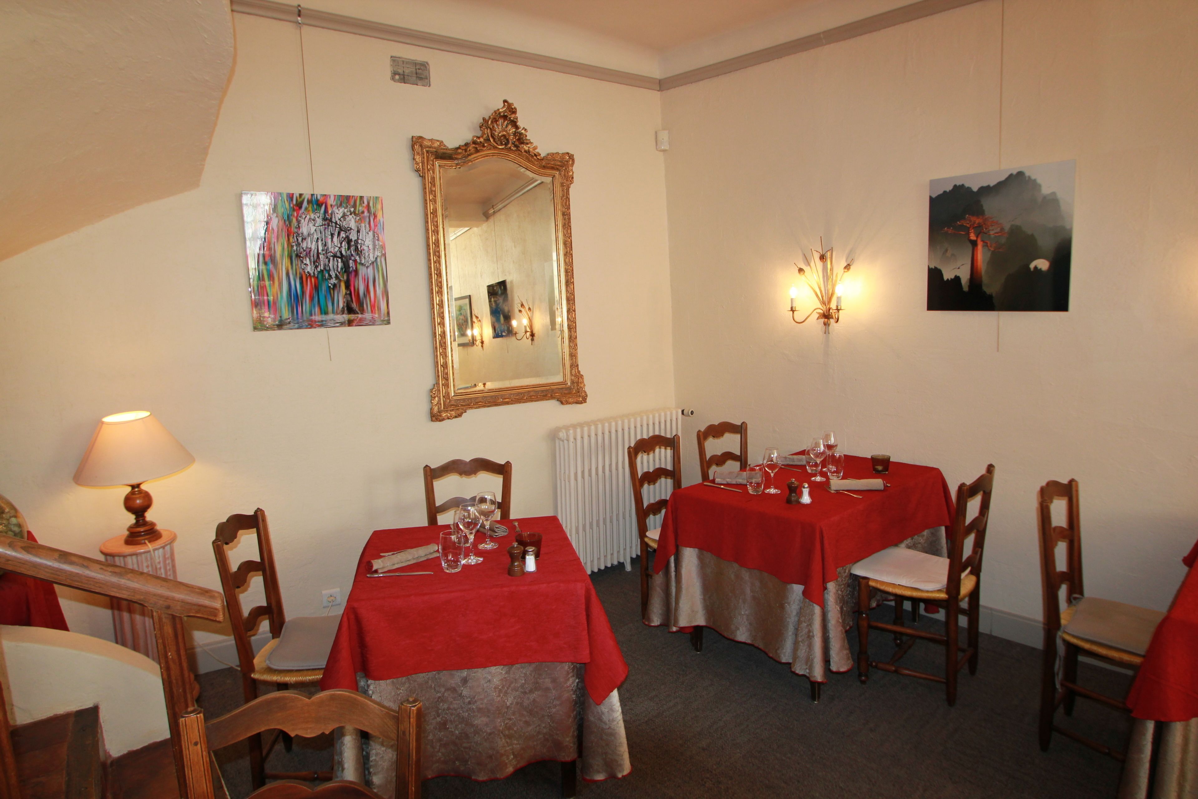 Ein Essbereich mit vier gedeckten Tischen, Stühlen, einem Spiegel und Wandbildern.