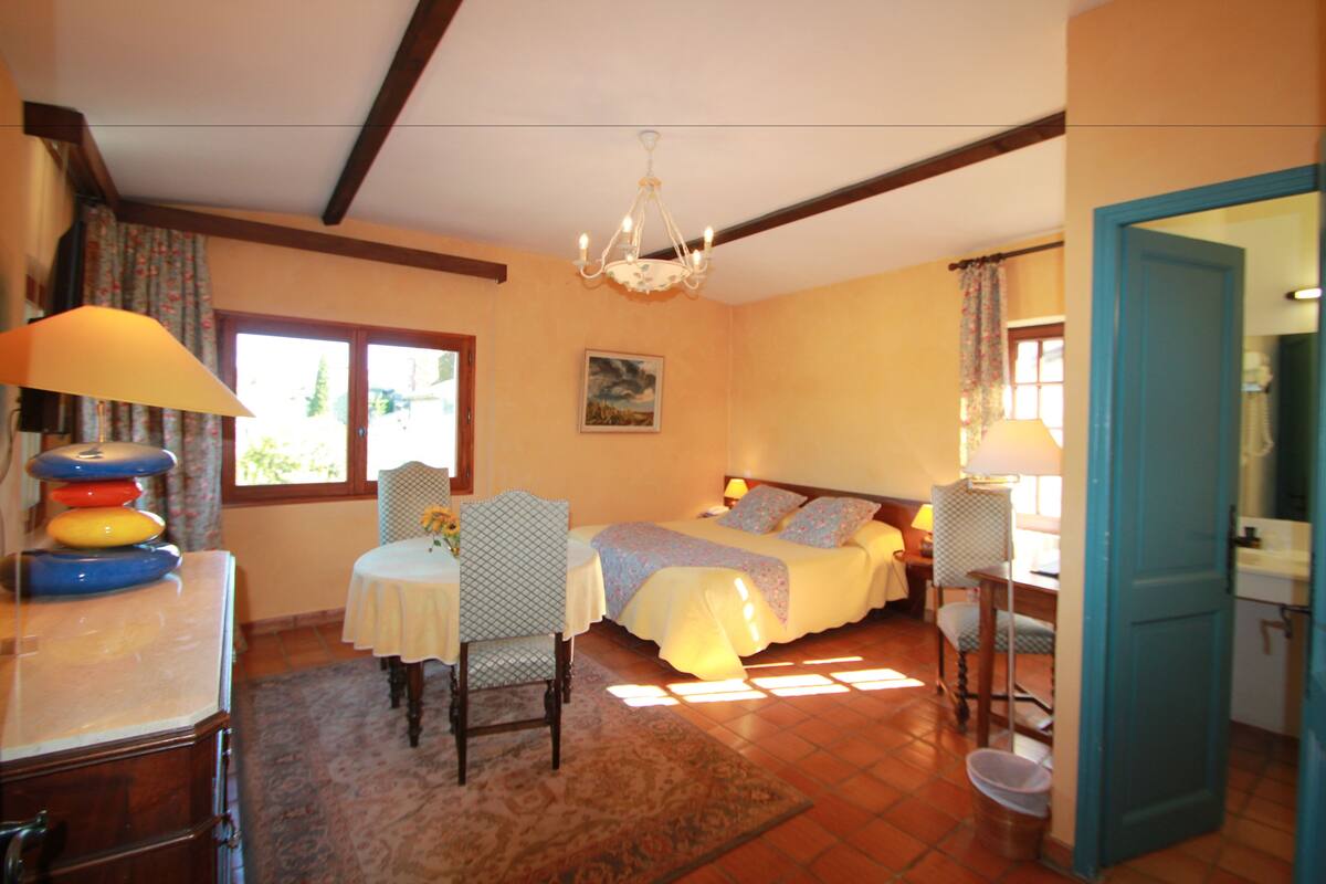 Une chambre à coucher avec un lit, deux tables de chevet, un lustre, une fenêtre et une vue sur l’extérieur.
