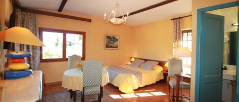 A bedroom with a bed, two bedside tables, a chandelier, a window, and a view of the outdoors.