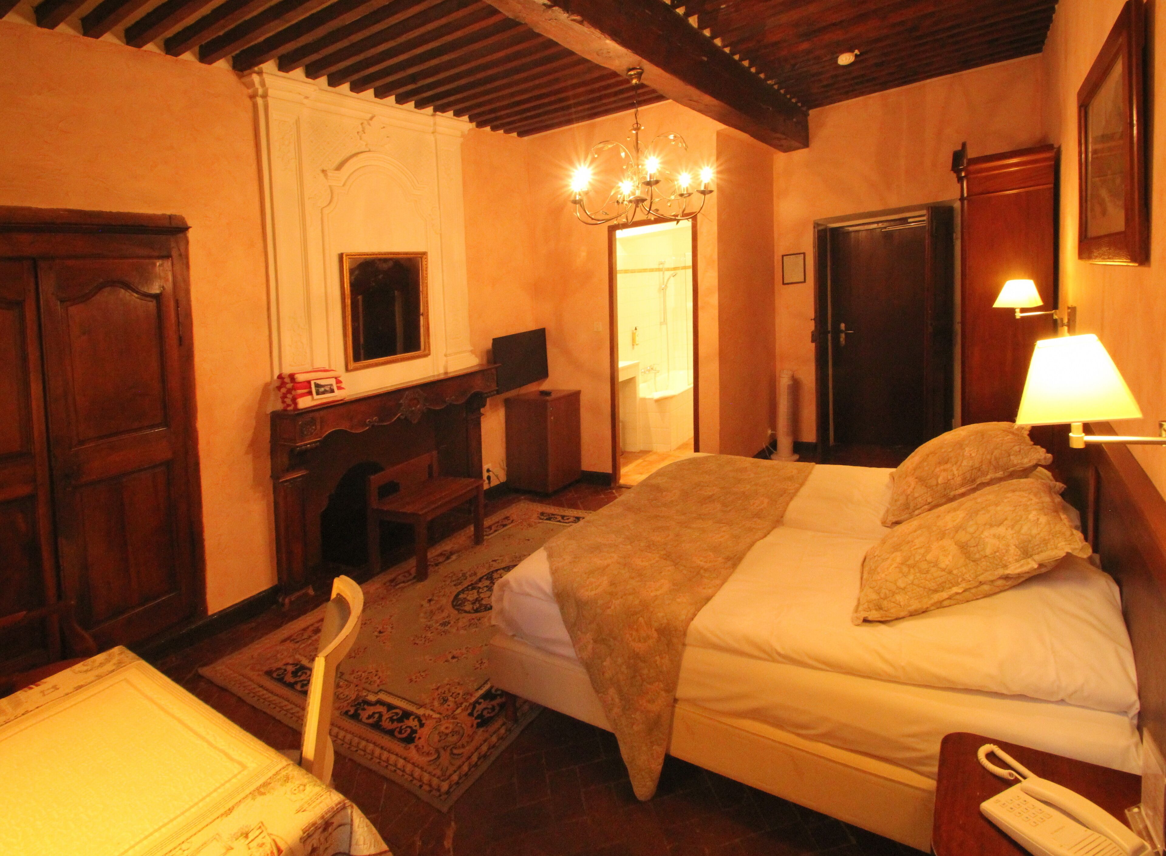 A bedroom with a bed, bedside table, lamp, and a wooden desk with a chair.