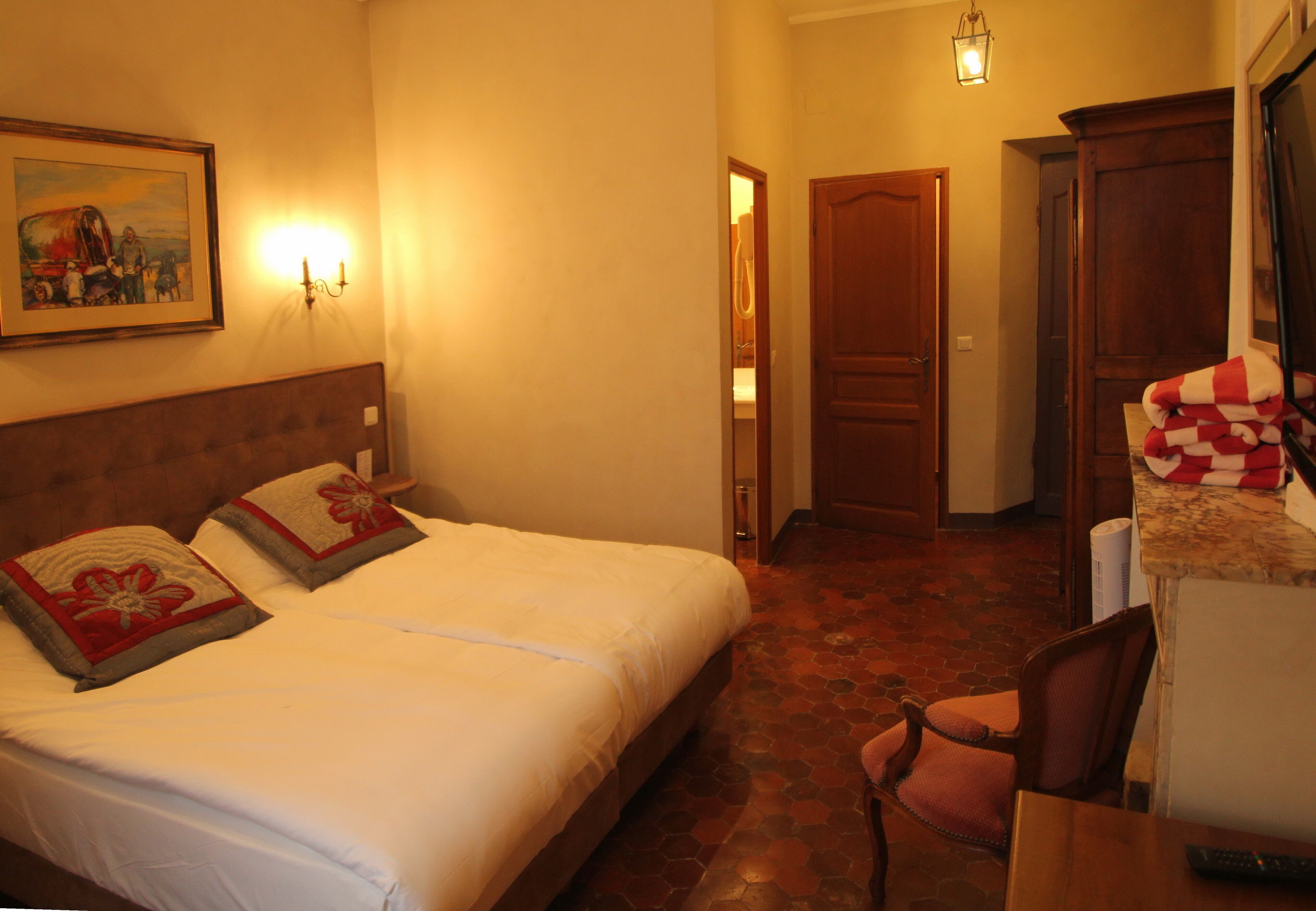 A hotel room with a bed, a chair, a desk, and a painting on the wall.